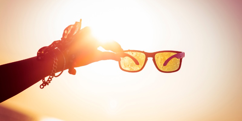 woman holding sunglasses towards sun